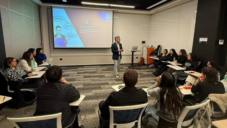 Jorge, de pie junto a una pantalla, presenta frente a un grupo de personas sentadas en una sala de capacitación